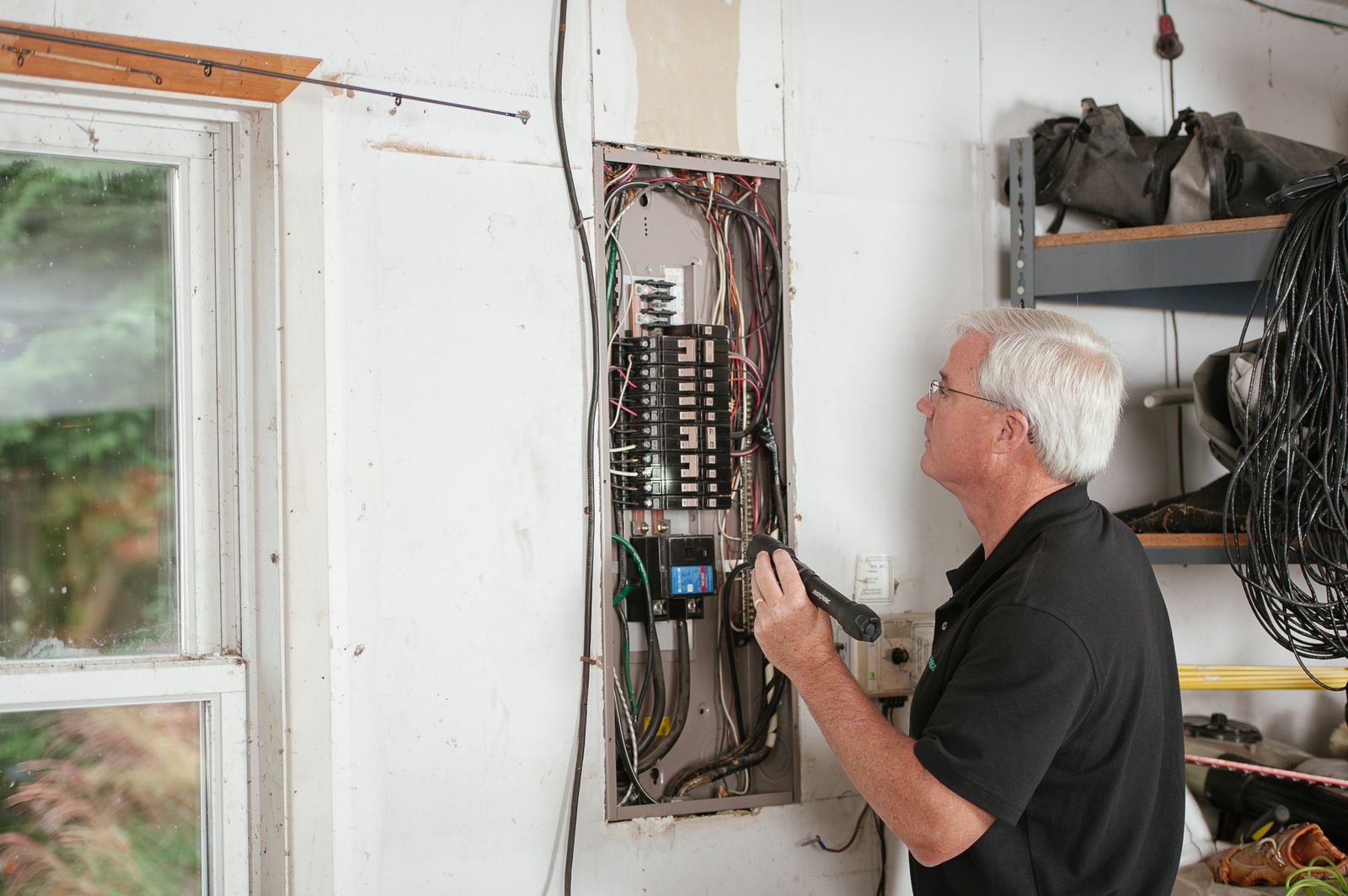 An inspector checks a residential electrical panel with a flashlight