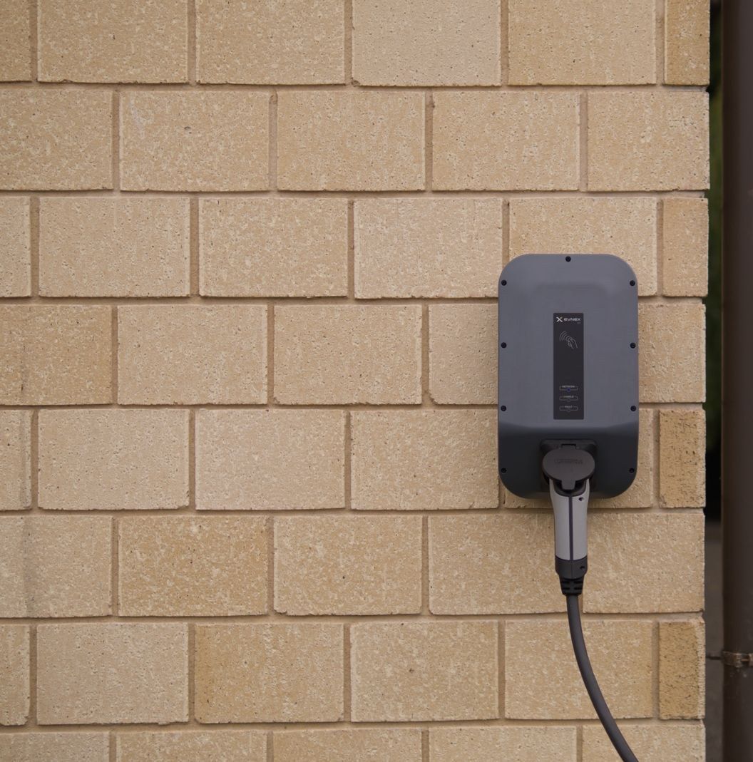A wall-mounted EV charging unit installed on a brick garage wall
