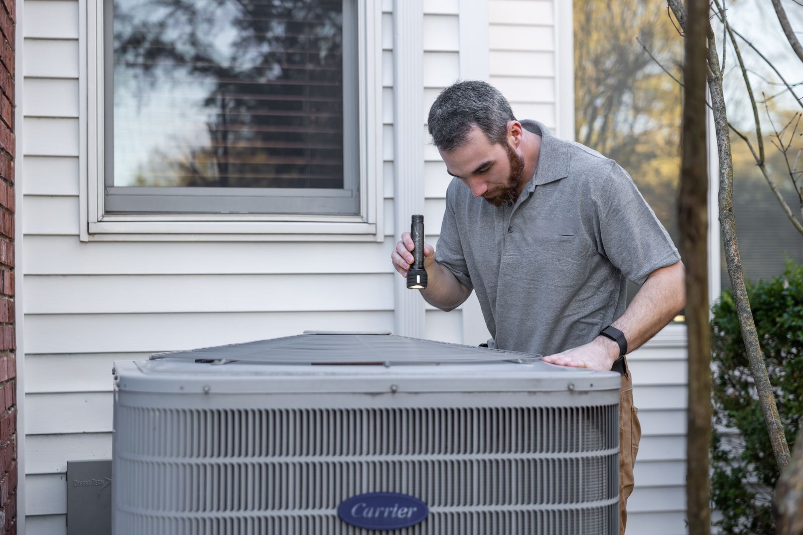 A technician inspects an outdoor air-conditioning condenser beside a house