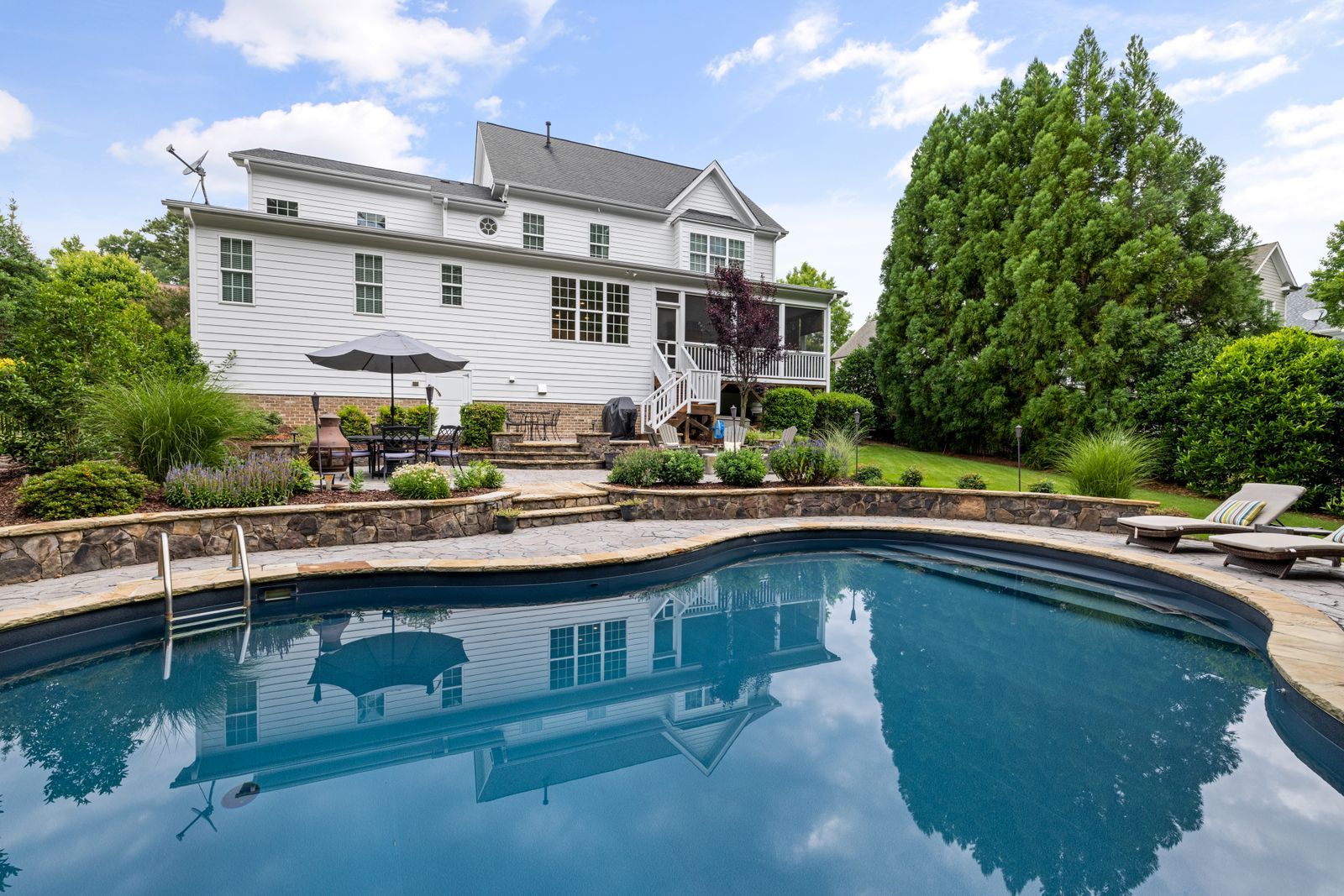 An in-ground pool and stone patio behind a two-story suburban house